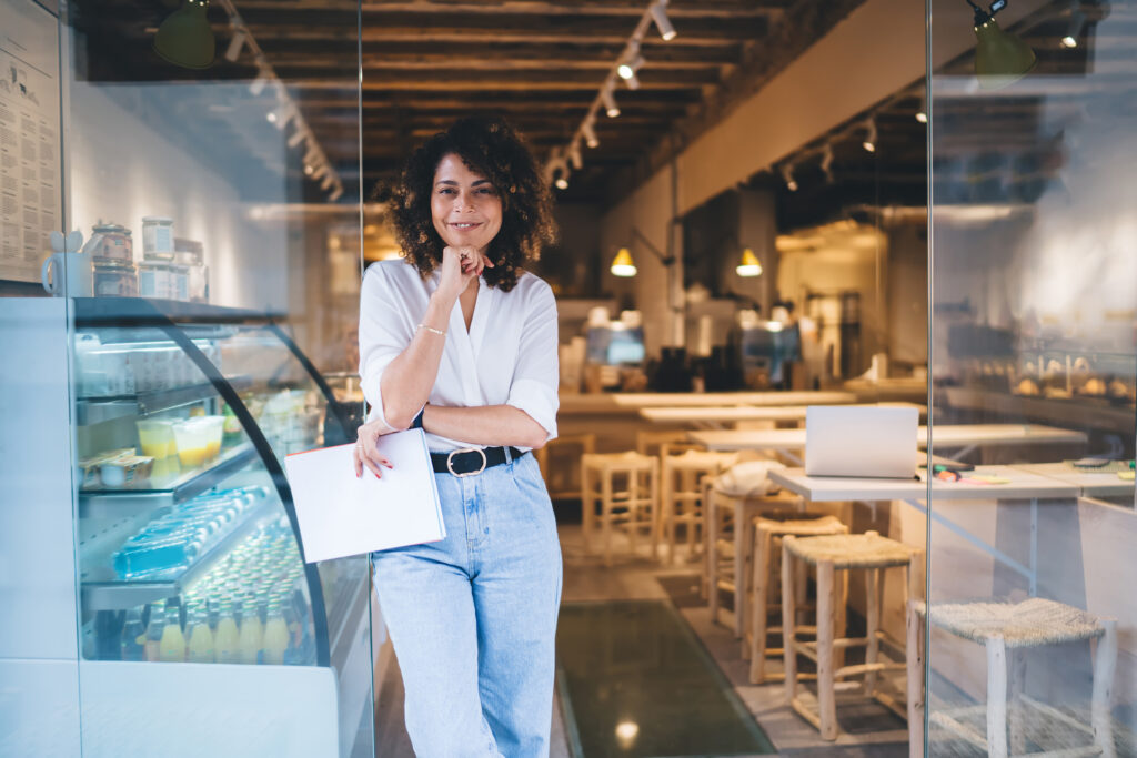 Gérante souriante appuyée à l'entrée de son café de quartier