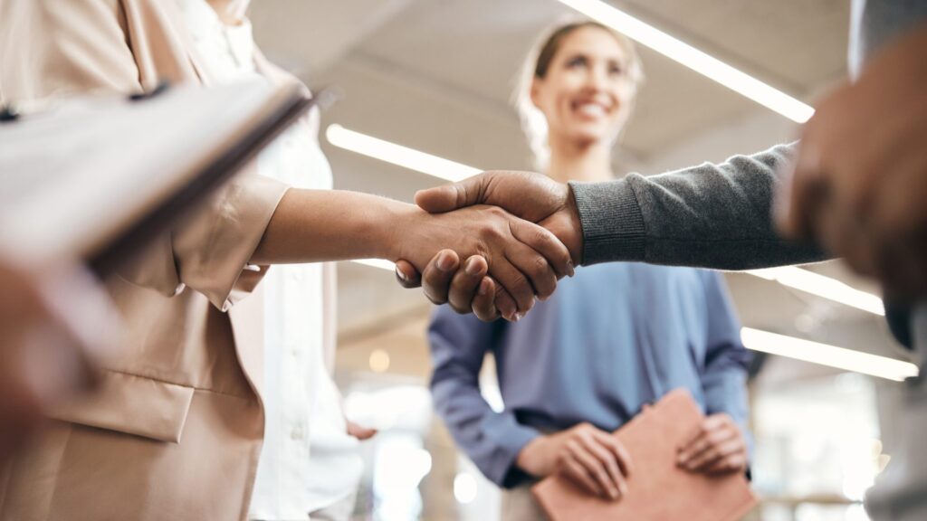 Poignée de main au début d'une entrevue, une recruteuse souriante en arrière-plan
