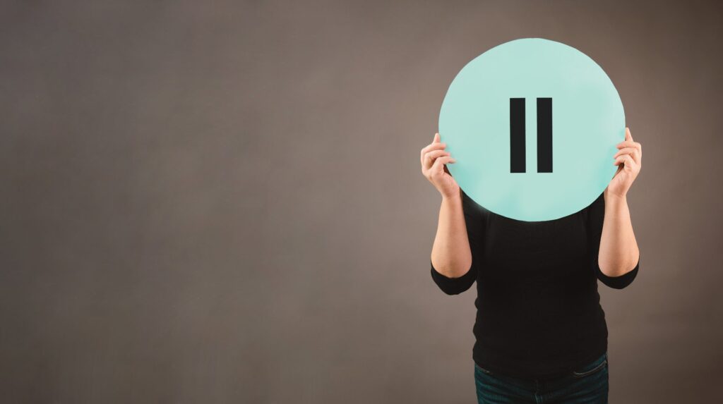 Personne tenant devant son visage un grand cercle turquoise affichant le symbole pause