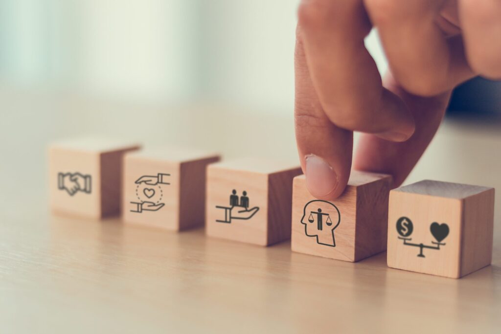 Main plaçant des cubes de bois illustrant l'entraide, la bienveillance, l'équipe, l'éthique et l'équilibre